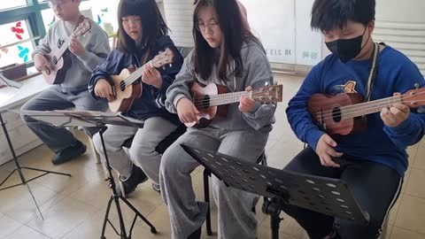 교실에서 악보를 보며 우쿨렐레를 함께 연주하는 학생들